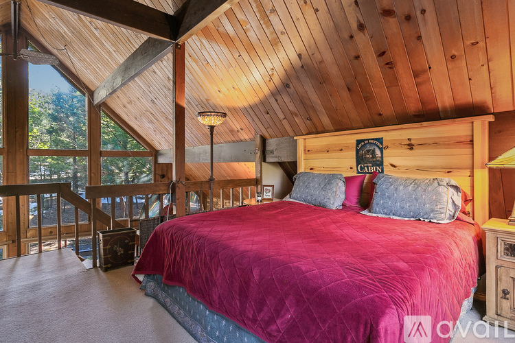 A bedroom with a red bedspread and wooden walls.