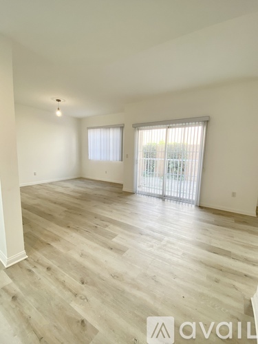 A spacious room with wooden flooring and a sliding glass door.