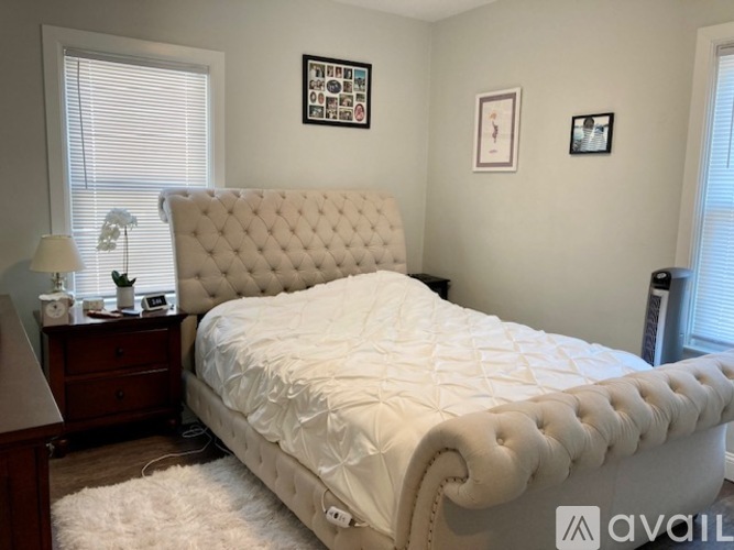 A white tufted bed with a white comforter and a white rug in front of it.