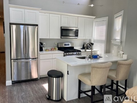 A kitchen with a stainless steel refrigerator, a microwave above the stove, and a white countertop with two chairs.