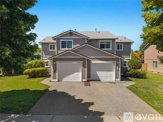 A two-story house with a garage is surrounded by a well-maintained lawn.