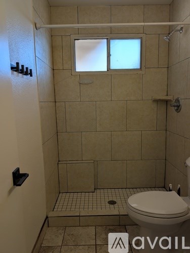 A bathroom with a toilet, tiled floor and walls, and a window.