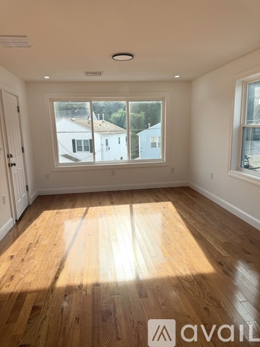 A room with wooden flooring and a window overlooking a house.