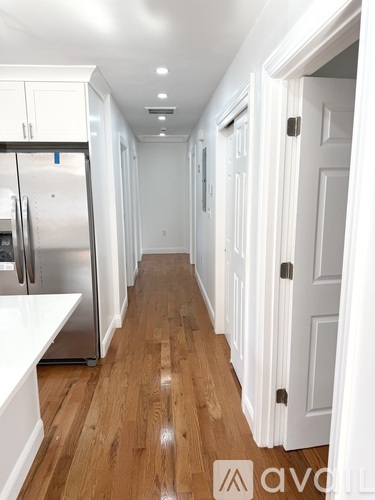 A long hallway with white doors and a stainless steel refrigerator.