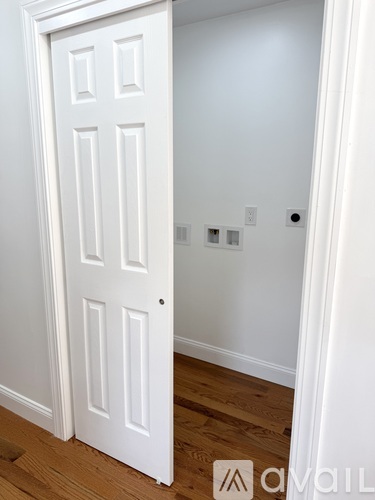 A white door is open to a room with wood flooring.