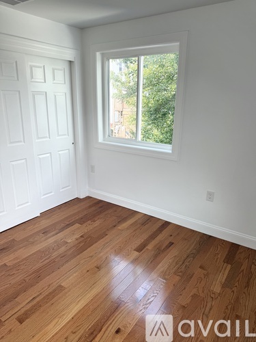 A room with a white door and a window with a view of trees.