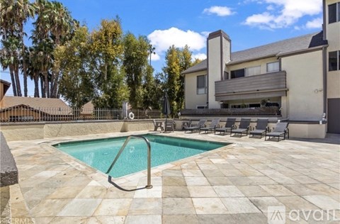 A swimming pool surrounded by a stone patio and lounge chairs.