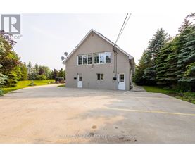 A two-story house with a garage is surrounded by trees and has a driveway in front.