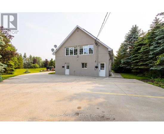 A two-story house with a garage is surrounded by trees and has a driveway in front.
