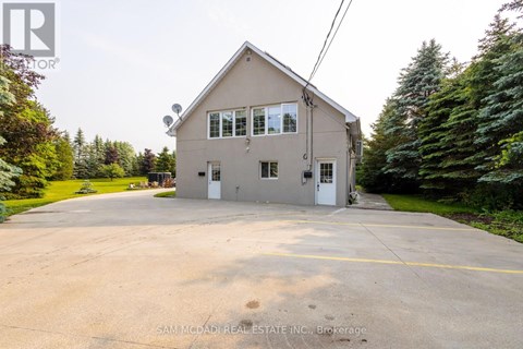 A two-story house with a garage is surrounded by trees and has a driveway in front.