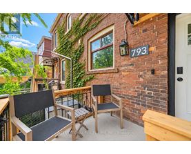 A balcony with a table and chairs is on the second floor of a brick building.