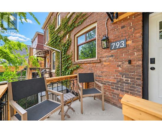 A balcony with a table and chairs is on the second floor of a brick building.