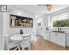 A white dining room with a table set for two and a painting of flowers on the wall.