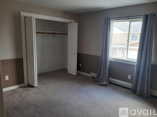 A bedroom with a large open closet and a window with curtains.