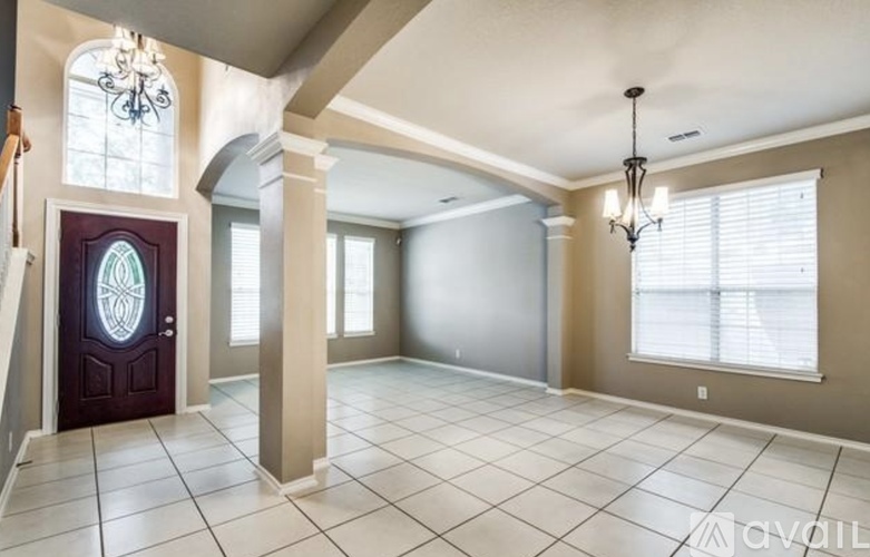A spacious room with a chandelier, a door with a stained glass window, and a tiled floor.