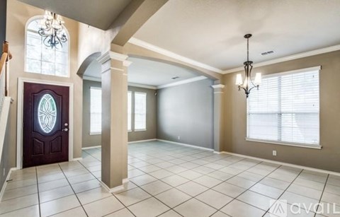 A spacious room with a chandelier, a door with a stained glass window, and a tiled floor.