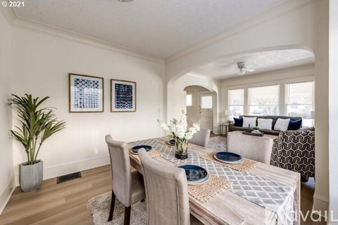 A dining room with a table set for two and a potted plant.