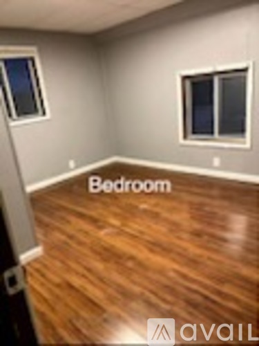 A bedroom with wooden flooring and two windows.