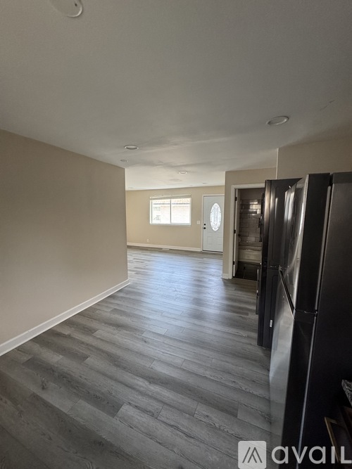 A kitchen area with a black refrigerator and wooden flooring.