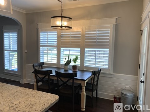 A dining room with a table, chairs, and a plant on the windowsill.
