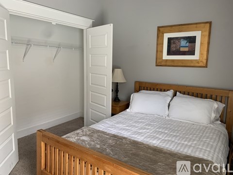 A bedroom with a bed, a nightstand with a lamp, and a picture frame on the wall.