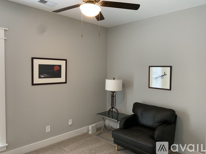 A living room with a black leather chair and a table with a lamp on it.