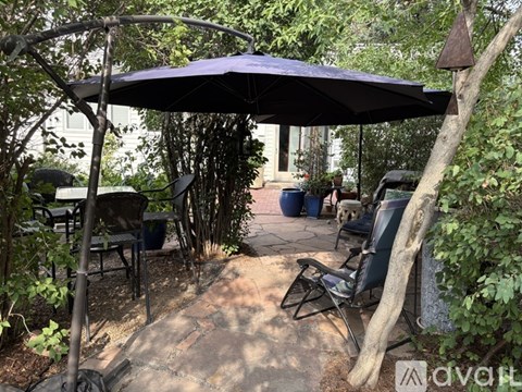 A patio with a black umbrella and chairs.