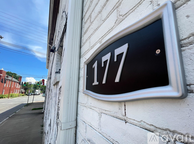 A black and white house number 177 mounted on a white wall.