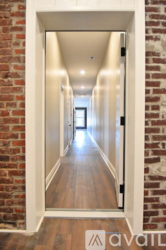 A hallway with a brick wall on the left and wooden floors.