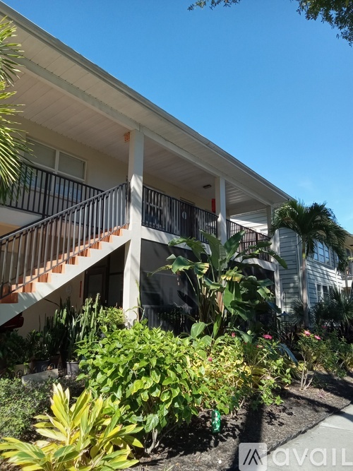 A white building with a balcony and plants in front.