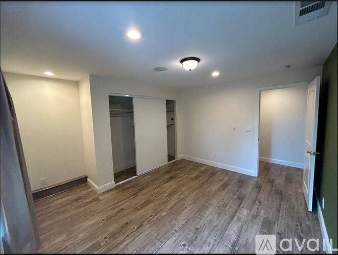 A room with wooden flooring and white walls, with a ceiling light and a window.