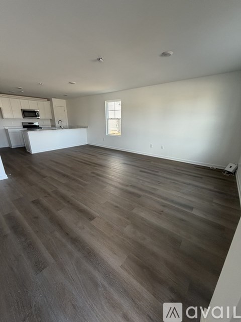 A spacious room with wooden flooring and a kitchen area in the background.