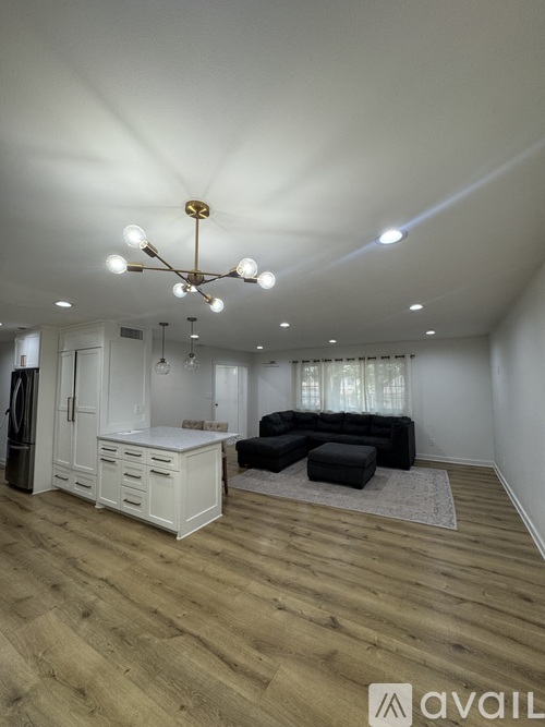 A living room with a white kitchen area and a black ottoman.