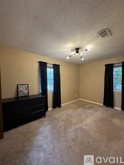 A bedroom with a bed, dresser, and window with black curtains.