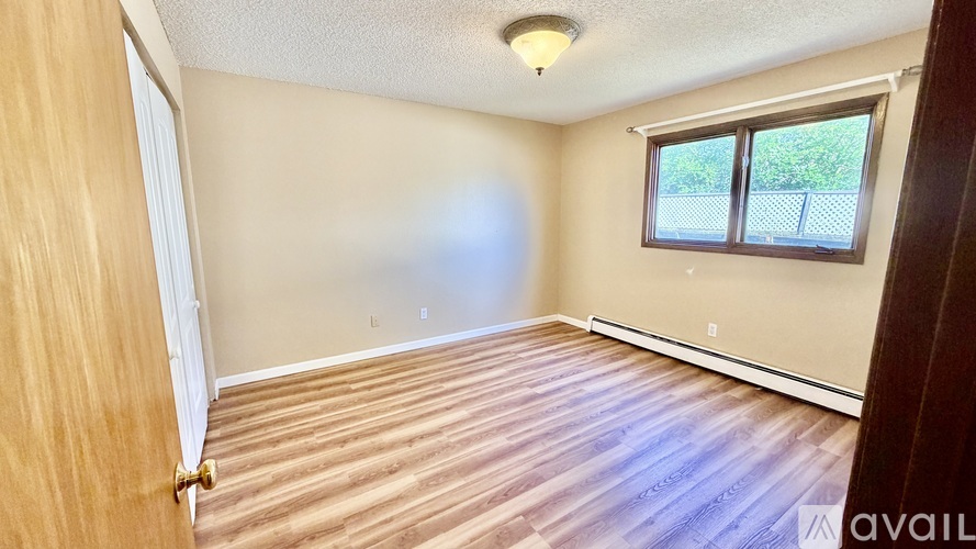 A room with wooden flooring and a window with a view of a fence.
