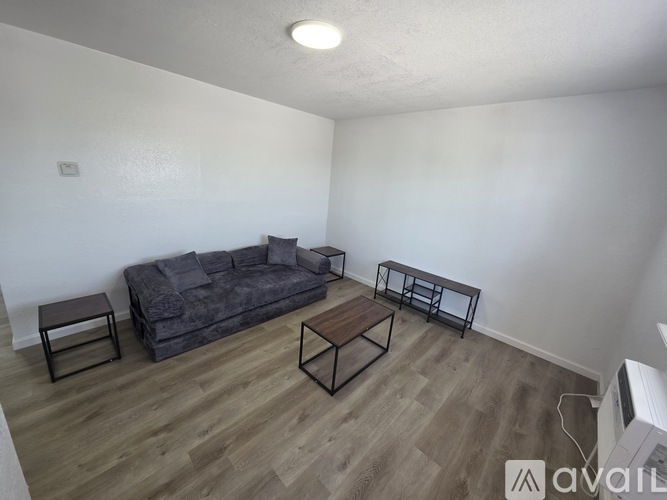 A living room with a grey couch, two black tables, and a wooden floor.