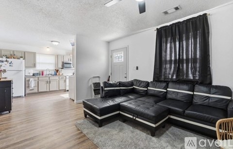 A black leather sectional sofa in a living room with a grey rug and a black chair.
