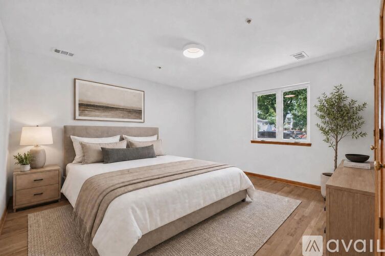 A bedroom with a large bed, a nightstand with a lamp, and a framed picture on the wall.