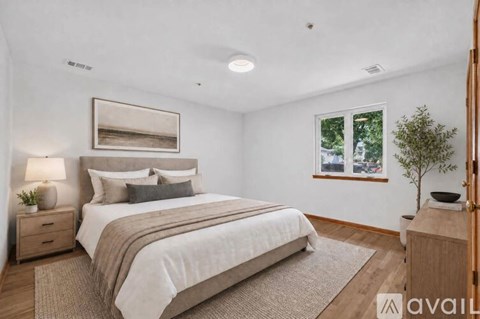 A bedroom with a large bed, a nightstand with a lamp, and a framed picture on the wall.
