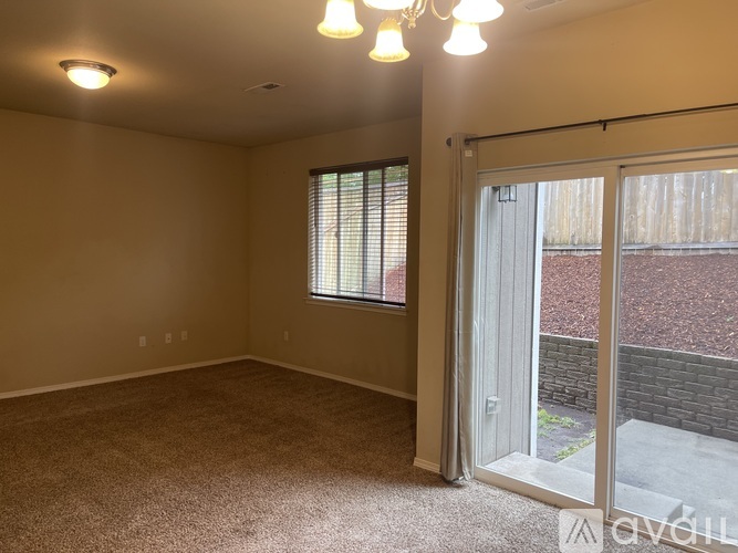 A room with a carpeted floor, a window with blinds, and a sliding glass door leading to a backyard.