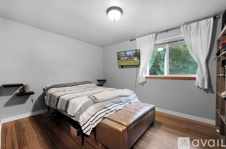 A bedroom with a bed, a window with white curtains, and a painting on the wall.