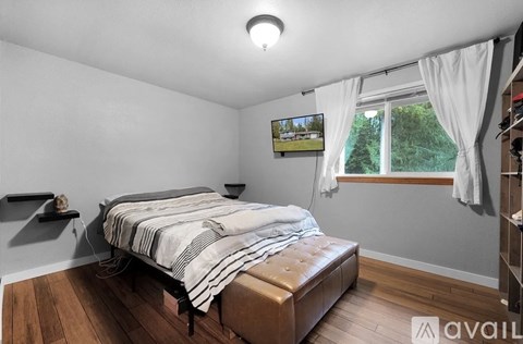 A bedroom with a bed, a window with white curtains, and a painting on the wall.