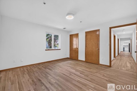 A room with wooden floors and white walls, with a painting hanging on the wall and a door on the right.
