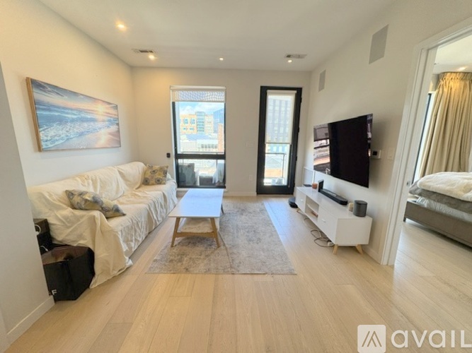 A spacious living room with a white sofa, a wooden coffee table, and a television on a white stand.