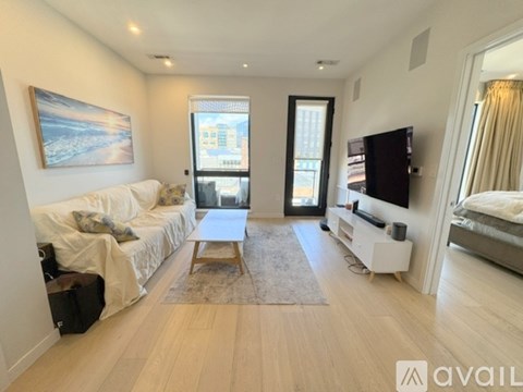 A spacious living room with a white sofa, a wooden coffee table, and a television on a white stand.
