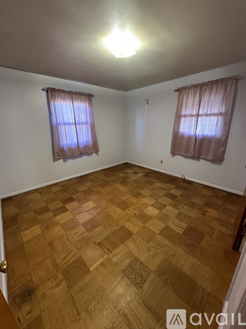 A room with wooden flooring and two windows with curtains.