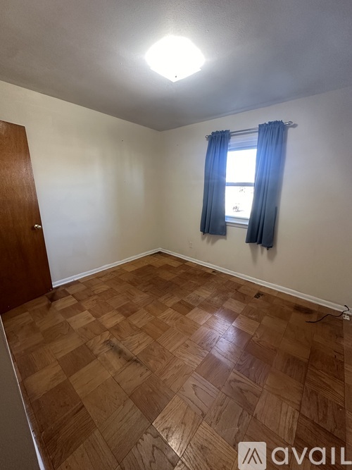 A room with wooden flooring and a window with blue curtains.