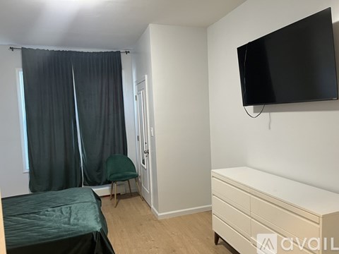 A bedroom with a bed, a chair, a dresser, and a flat-screen TV mounted on the wall.