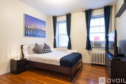 A bedroom with a large bed, a painting on the wall, and a window with curtains.