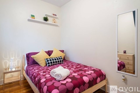 A bedroom with a bed covered in a pink and purple polka dot comforter.